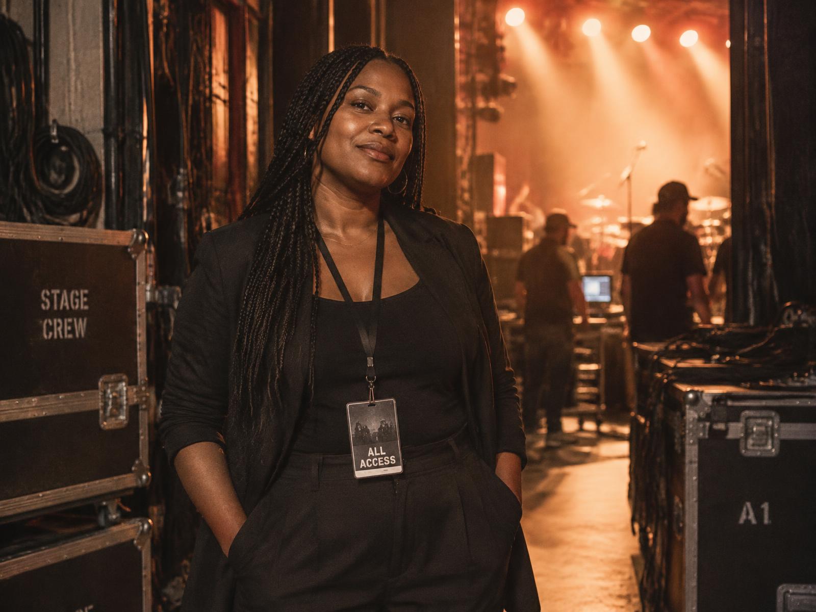 A Black woman creative director standing backstage before a performance, wearing an all-access pass